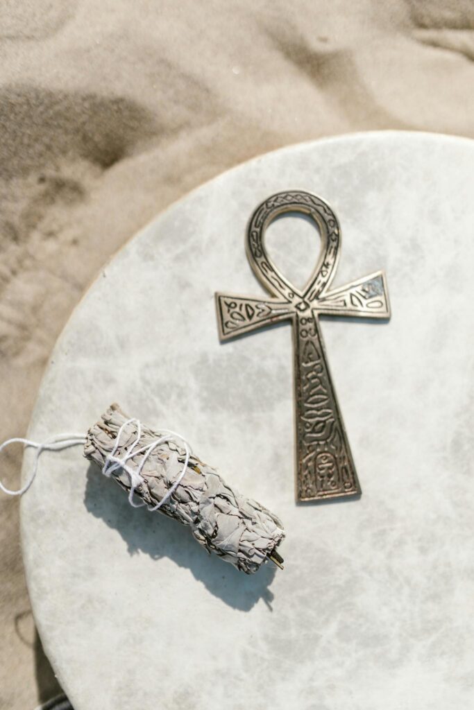 A detailed ankh symbol with sage bundle on a textured sandstone surface, evoking spiritual themes.