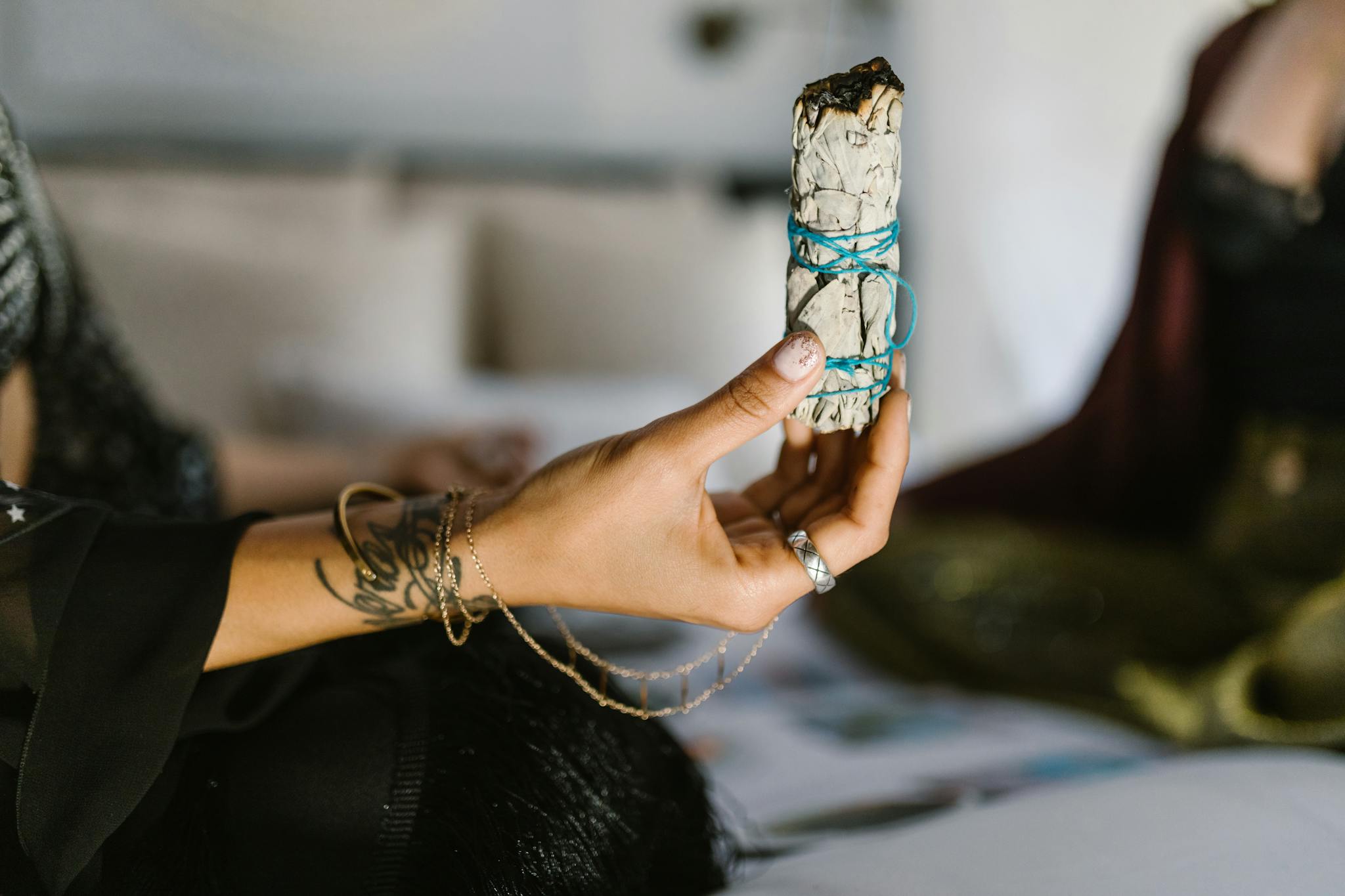 A person holding a sage bundle tied with blue string, often used in spiritual cleansing rituals.