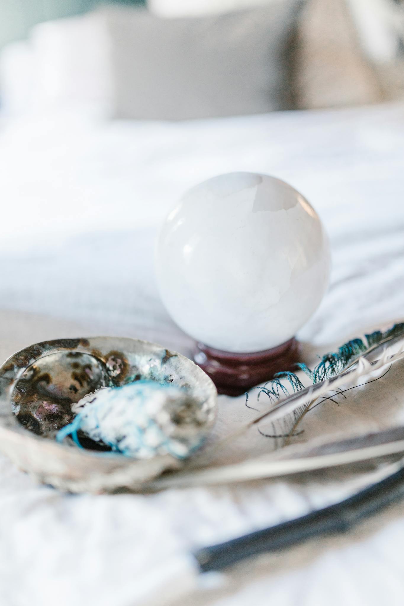 Crystal ball and feather with smudging tools on a soft surface, ideal for spiritual and mystical themes.